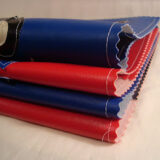 Stacked rolls of colorful fabric in red and blue with a black and white design on top, perfect for creating a stylish notebook cover, displayed against a plain background.