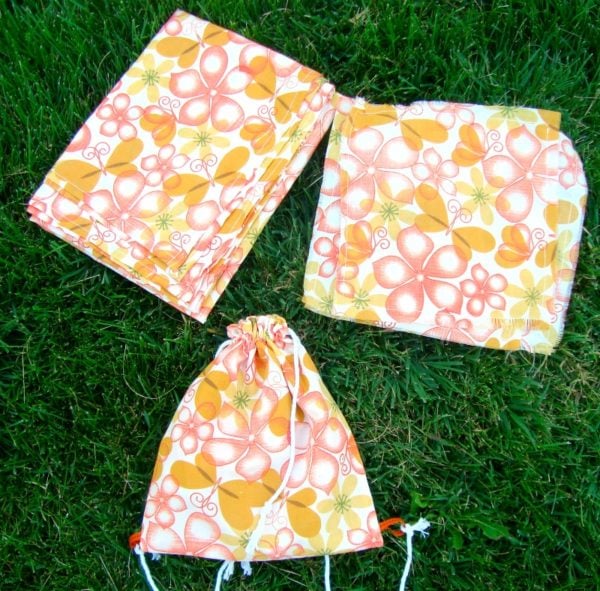 a cinch bag, napkins and a tablecloth folded and on grass. this set is perfect for little kids to spend some time outside for snacks or lunch