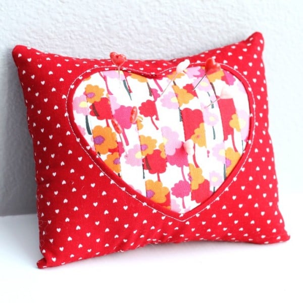 A red rectangular pincushion with small white hearts features a large heart-shaped patch with a floral pattern in the center. Perfect for storing pins, it&rsquo;s inspired by Free Pincushion Patterns for crafty sewing enthusiasts.