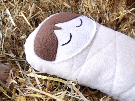 Swaddle Doll with eyes embroidered and closed and brown fleece hair laying on hay