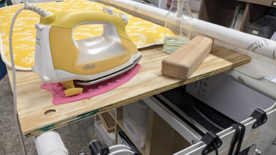 oliso iron and clapper on a wood iron board that is laid on a long arm bars