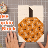 A pair of hands holds a pumpkin-themed quilt block on a cutting mat. The block features an orange fabric with floral patterns, perfect for a fall table runner. Surrounding it are a pincushion, rotary cutter, and fabric pieces. Text reads "FREE Pumpkin Quilt Block".