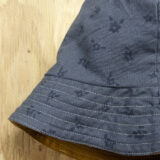 A reversible bucket hat with a subtle floral pattern hangs on a wooden surface. The brim is lined with contrasting yellow fabric inside, adding a pop of color to the thoughtful design.