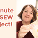 A person is holding a piece of patterned fabric with a smile, next to text reading, "5 Minute NO SEW project!" In the background, colorful quilted patterns decorate the wall. Perfect for creating a fabric-covered mouse pad in minutes—check out our quick how-to video!.