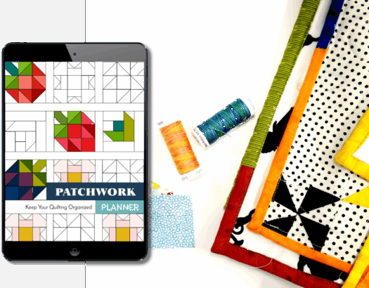 digital patchwork planner on an ipad screen next to thread and quilts on a table