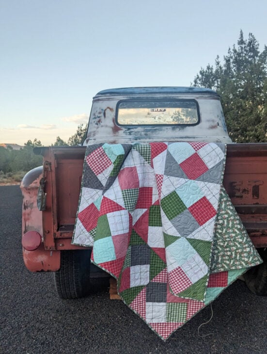 Simple Jelly Roll Race Quilt Tutorial 4 red, green and white christmas fabric in a quilt hanging on a vintage truck. the block is a four patch on point