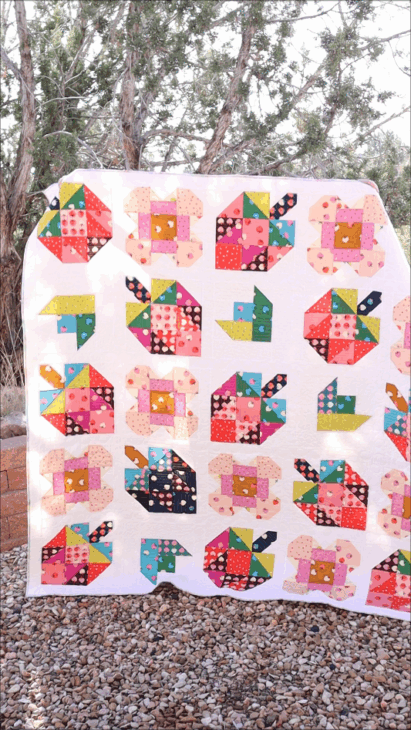 A colorful patchwork quilt with animal shapes, including cats, dogs, and birds, is displayed outdoors against a backdrop of trees and stones&mdash;a delightful inspiration for quilters using their favorite Patchwork Planner.