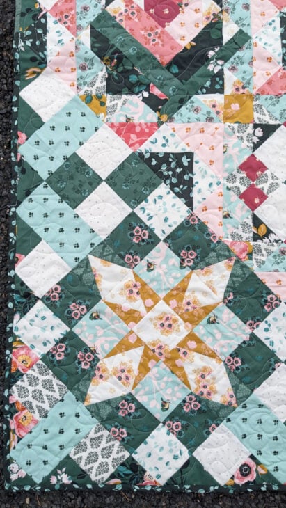 Hidden Gems Block of the Month Finishing 4 A colorful quilt featuring geometric patterns with floral fabrics in green, yellow, pink, white, and teal. Part of the Hidden Gems Block of the Month, it showcases star and diamond shapes plus intricate quilting throughout.
