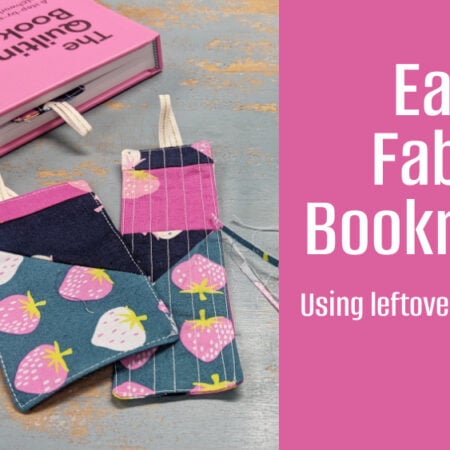 A pink book lies open with two colorful DIY fabric bookmarks—one with a strawberry pattern, the other with pink stripes—on a gray surface. Text reads: "Easy Fabric Bookmarks - Using leftover quilt blocks and easy sewing!.