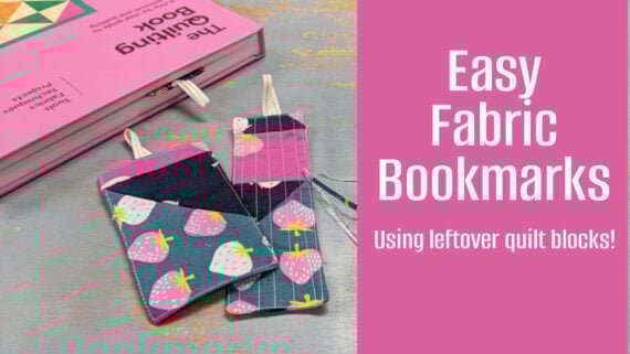 A pink book lies open with two colorful DIY fabric bookmarks—one with a strawberry pattern, the other with pink stripes—on a gray surface. Text reads: "Easy Fabric Bookmarks - Using leftover quilt blocks and easy sewing!.