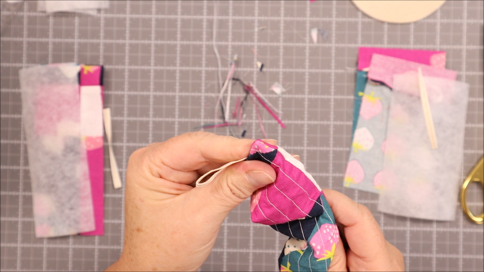 Fast & Easy DIY Fabric Bookmark | Use Up Leftover Quilt Blocks! 15 A person’s hands sew two pieces of colorful fabric together over a gridded cutting mat, with quilt blocks, a pair of gold scissors, and more fabric pieces scattered around.