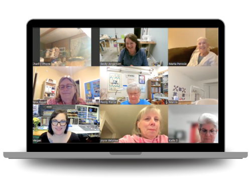 A laptop screen displays a virtual meeting with nine women in separate video call windows, each in different home settings, smiling and engaging with one another.
