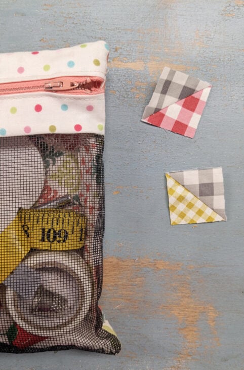 Mesh Front Zipper Project Bag Tutorial 18 A mesh zipper bag holds sewing supplies, perfect for any Zipper Bag Tutorial. Three small square quilt fabric pieces in red, yellow, and gray patterns are displayed on a distressed blue wooden surface beside the pouch.
