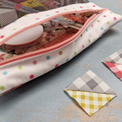 A polka dot zippered pouch, perfect for a zipper bag tutorial, holds sewing supplies on a blue surface beside two small quilt pieces in gray-yellow and gray-pink gingham, showcasing charming quilt block inspiration.