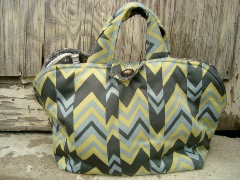 A fabric handbag with yellow, grey, and light blue chevron patterns&mdash;perfect for your next Make and Take or Monthly Sewing project&mdash;features two handles and a button closure, set against a weathered wooden background.