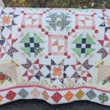 A colorful handmade quilt, inspired by the Starlit Meadow Block of the Month 2026, features vibrant star and square patterns in green, orange, pink, and blue fabric, draped over the side of a rustic vehicle outdoors.