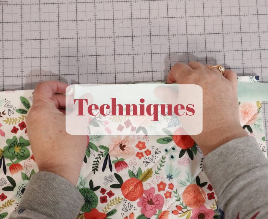 A person folds the edge of a floral fabric on a gridded cutting mat. The word "Techniques" appears in red text on a white box overlay.
