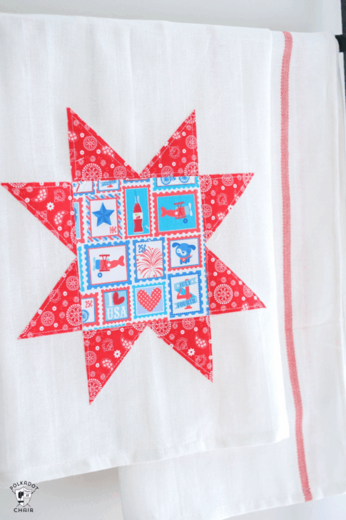 10 Patriotic Flag Projects to Sew Before the 4th of July 12 A white tea towel with a red star quilt pattern—ideal for Patriotic flag projects or the 4th of July—features blue, red, and white patchwork squares in the center and hangs on a rod. Another plain white towel with red stripes is partially visible behind it.