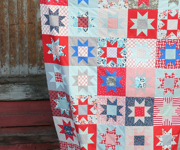 10 Patriotic Flag Projects to Sew Before the 4th of July 13 A colorful patchwork quilt featuring red, blue, and white star patterns, perfect for patriotic flag projects or to sew for the 4th of July, hangs in front of a rustic wooden wall with peeling paint.