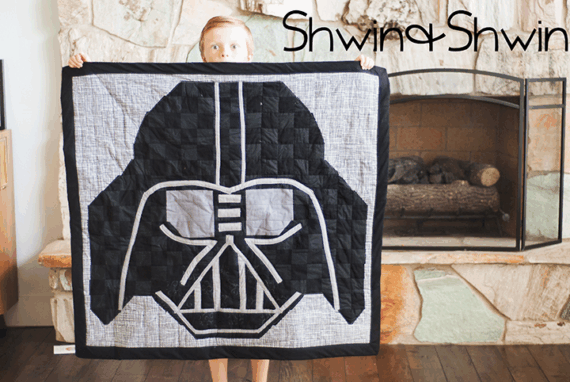 A child stands indoors holding a quilt with a large Darth Vader mask design&mdash;perfect for Star Wars fans. A stone fireplace is in the background. The words "Shwin & Shwin" appear in the top right corner.