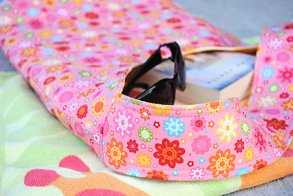 Sew Your Own Beach Bag or Tote with These Free Patterns 4 A close-up of a pink floral-patterned tote beach bag resting on a colorful towel, with sunglasses and a book partially visible inside the bag.
