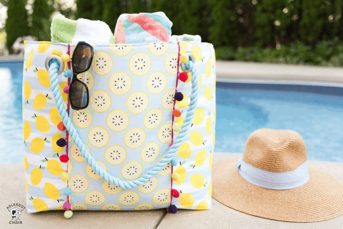 Sew Your Own Beach Bag or Tote with These Free Patterns 9 A colorful poolside scene with a lemon-patterned beach tote holding towels and sunglasses, next to a straw sunhat with a white band, all set beside a swimming pool—perfect inspiration for creating your own with free patterns.