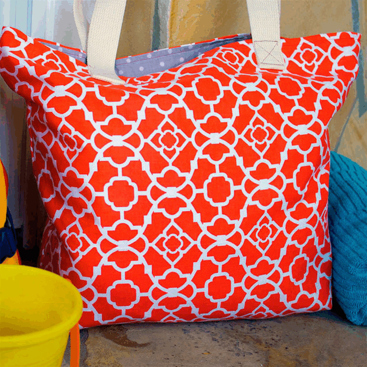 Sew Your Own Beach Bag or Tote with These Free Patterns 11 large geometric red and white fabric print bag with white ribbon handles sitting on tile with a beach towel and bucket for sand