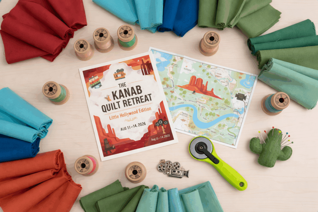 A flat lay of colorful fabric rolls, spools of thread, a map, a Southern Utah Quilt Retreat flyer, a green rotary cutter, metal charms, and a small cactus pincushion arranged on a light wooden surface.