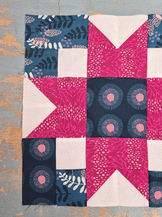 Christmas Quilt Block Swap - sign up is open! 2 A quilt block swap gem featuring geometric patterns in pink, blue, and white fabrics. The design showcases a pink star with floral prints, blue circles with white dots, and leaf motifs, all set on a distressed wooden surface.