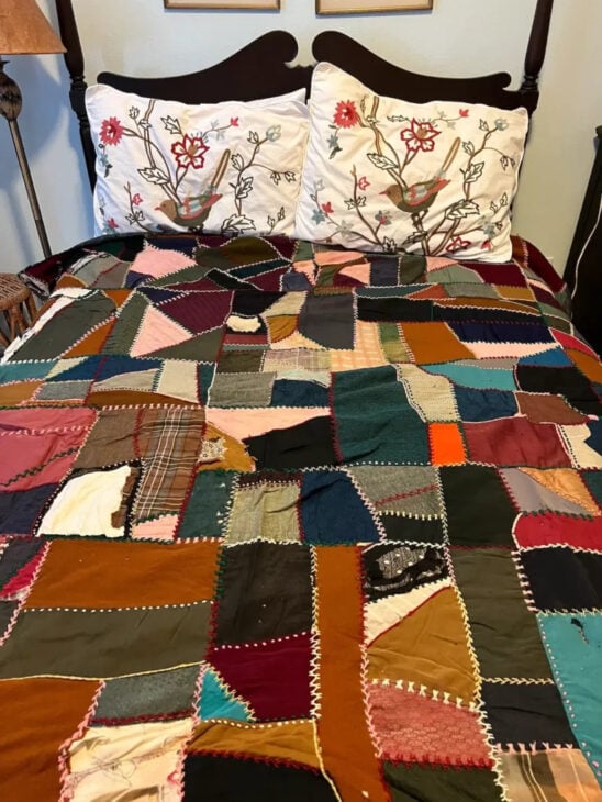25 Must Sew Scrappy Strip Quilt Patterns 11 A bed with two floral-patterned pillows and a colorful patchwork quilt, inspired by scrappy strip quilt patterns, features various fabric pieces and decorative stitching for a vibrant, homemade look.