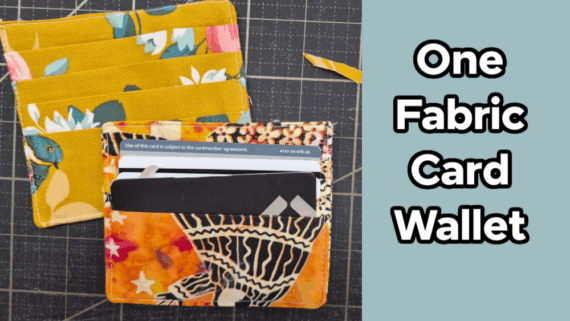 Two colorful fabric card wallets, one yellow with floral patterns and one orange with abstract designs, are displayed on a cutting mat. The text "One Fabric Card Wallet" appears on a blue background to the right, showcasing an easy to sew card wallet pattern.