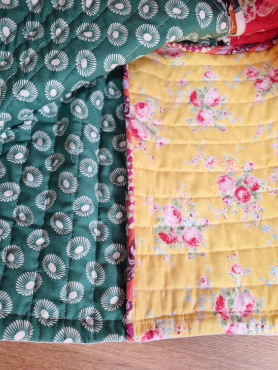 A close-up of a quilt with two different patterns&mdash;ideal as a Sewing Machine Cover. One side is green with white circular designs; the other is yellow with a floral print featuring pink and white flowers. The quilt rests on a wooden surface.