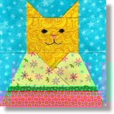 A colorful cat quilt block features a yellow cat with a patterned face, wearing a floral dress. The blue background has white stars, while the dress pops with pink, green, and yellow patterns.