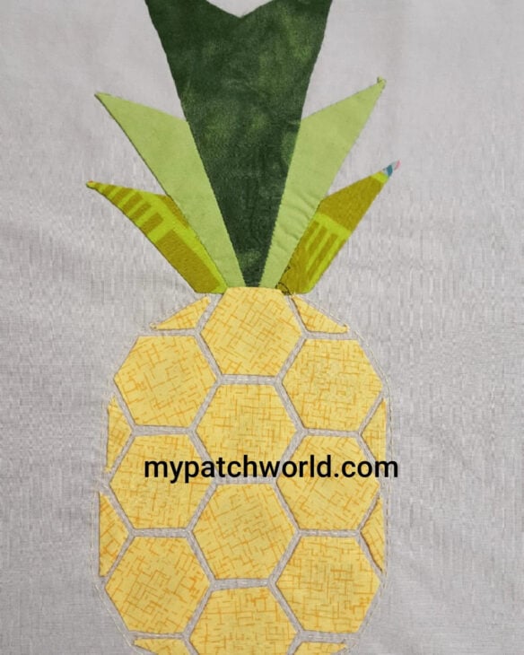 A fabric quilt block featuring a pineapple made from yellow hexagons for the fruit and green triangular leaves, with "mypatchworld.com" printed on the pineapple. Try our free sewing tutorial to sew pineapple quilt blocks just like this!.