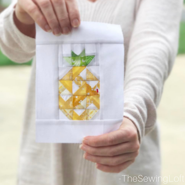 A person in a light sweater holds up a quilt block featuring a patchwork pineapple design made with yellow and green fabric on white, perfect for anyone wanting to learn to sew or create their own pineapple quilt blocks.