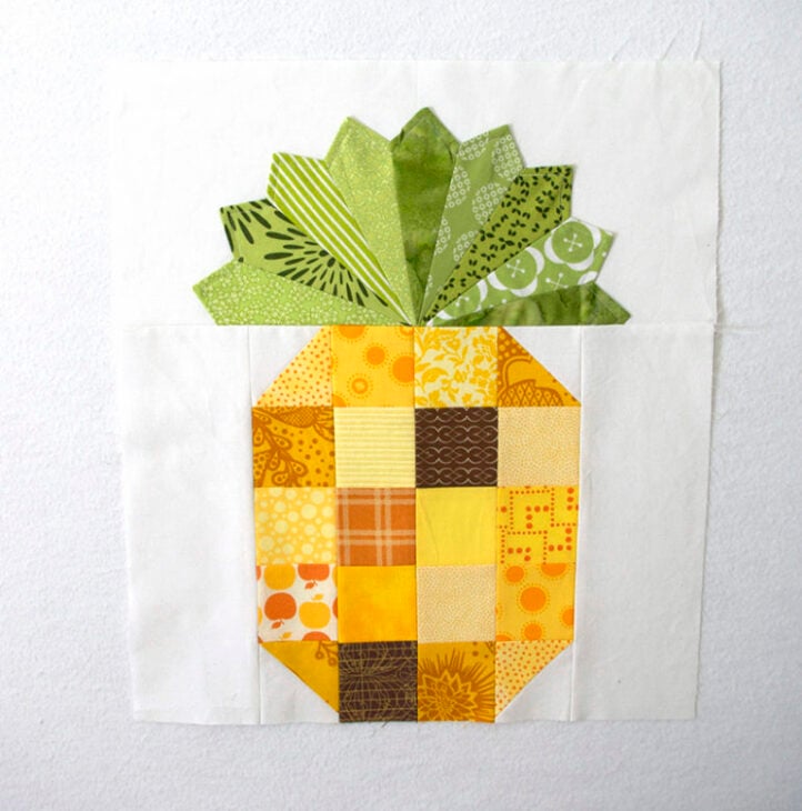 Create a Pineapple Quilt block featuring yellow and orange patterned squares for the fruit and green pieces for the leaves, all on a white background. Use our Free Sewing Tutorial to easily sew Pineapple Quilt Blocks at home.