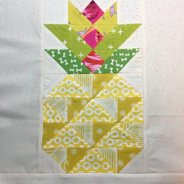 A quilt block depicting a pineapple, made with geometric fabric pieces in yellow, green, and pink patterns on a white background with small pink dots&mdash;perfect for those wanting to learn to sew pineapple quilt blocks.