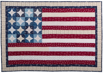 A handmade quilt inspired by the American Flag, featuring blue and white star-patterned blocks in the top left and red and white striped sections, all crafted with intricate stitching and patterned fabrics.