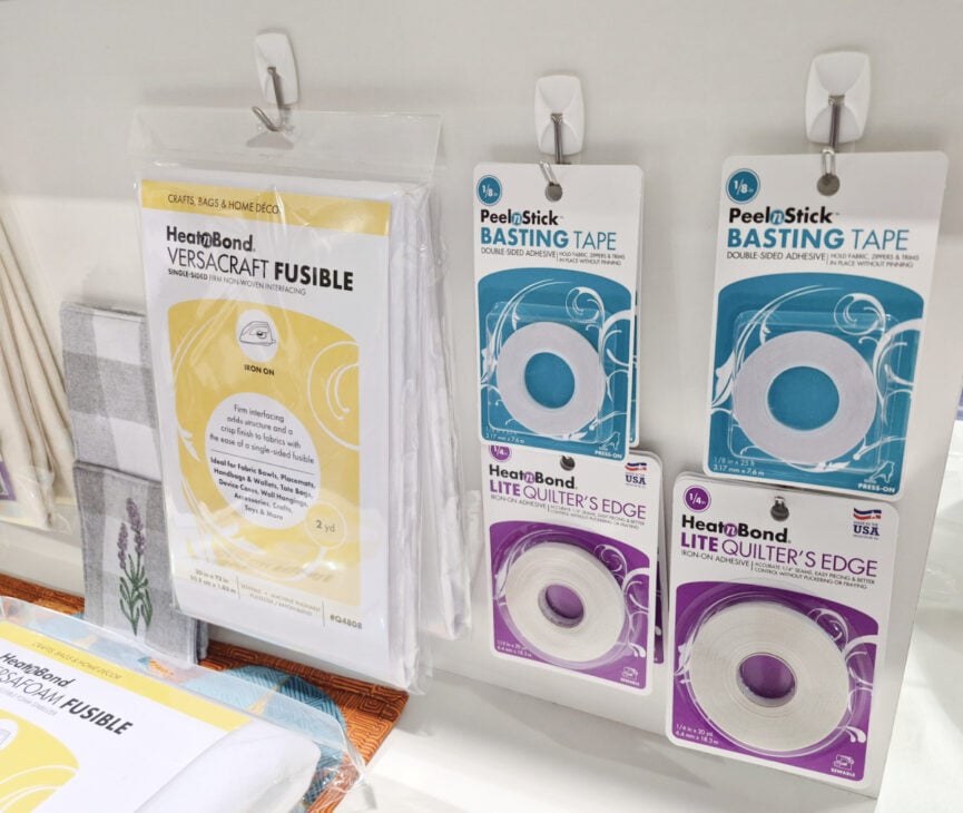 H+H Americas Swag & Walk the Floor with me 3 A display of sewing supplies at H+H Americas features HeatnBond VersaCraft Fusible fabric sheets, two sizes of Peel n Stick Basting Tape, and HeatnBond Lite Quilter’s Edge double-sided adhesive tape—perfect for grabbing some creative swag as you Walk the Floor.