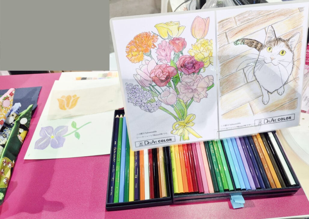 H+H Americas Swag & Walk the Floor with me 9 A set of colored pencils on a pink table with two coloring pages—one of a bouquet and one of a cat—displayed upright, plus two watercolor flower paintings laying flat, perfect H+H Americas swag for anyone ready to walk the floor.