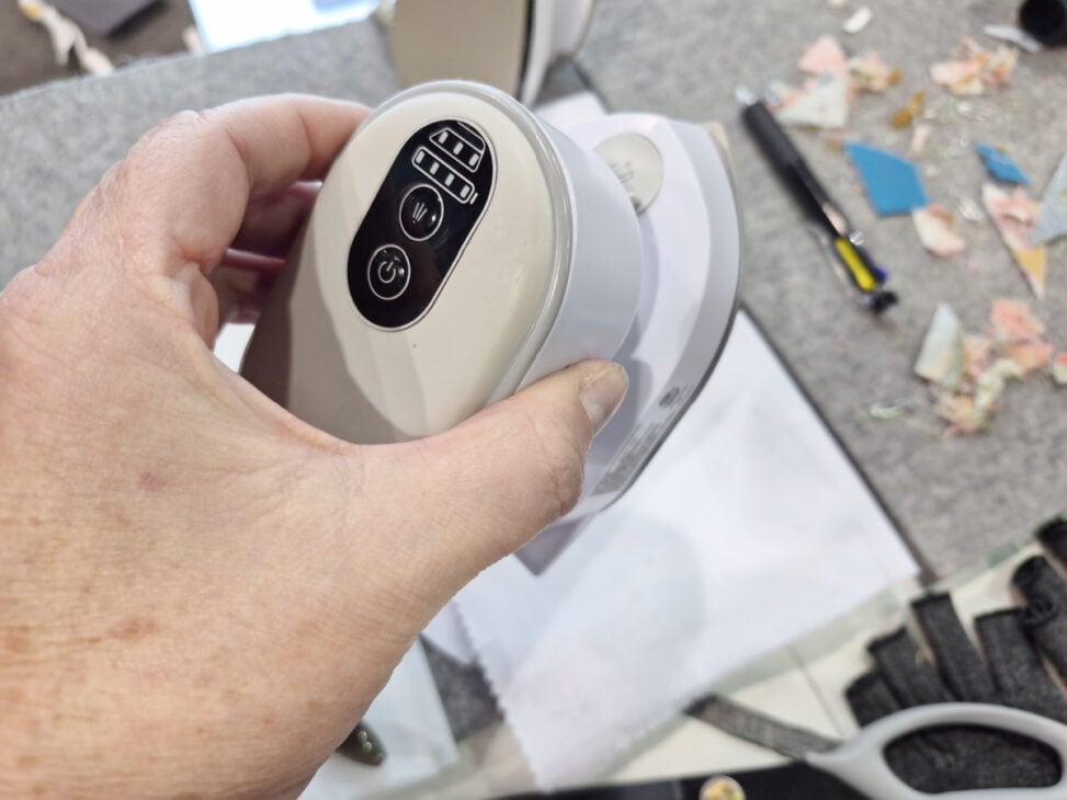 H+H Americas Swag & Walk the Floor with me 5 A hand holds an electronic device with control buttons, including a power button and numbered settings, while various tools and H+H Americas swag are scattered on the work surface in the background.
