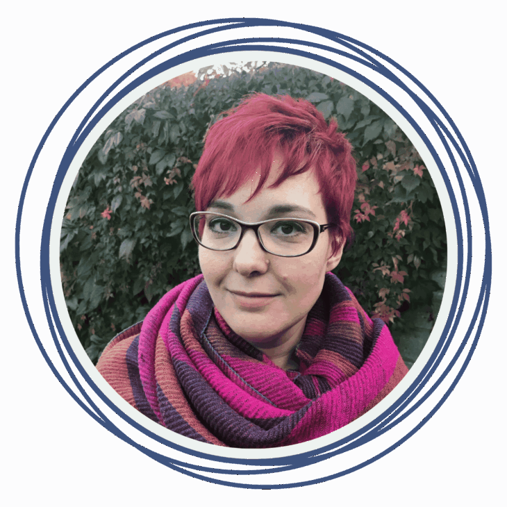 A person with short red hair and glasses, wearing a colorful striped scarf, stands outdoors in front of green foliage. Overlapping blue circles frame the image, echoing patterns from a quilting summit or inspiring ways to move the needle in creativity.