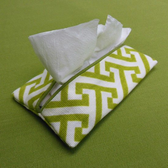 A green and white travel tissue holder with stylish tissue holder patterns, featuring tissues protruding and placed on a matching green surface.