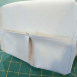 A close-up of a partially sewn fabric piece with two pockets on one side, sitting on a green cutting mat with a grid pattern. Loose threads are visible around the edges, making it perfect for a sewing tutorial on how to Sew Box Corners.