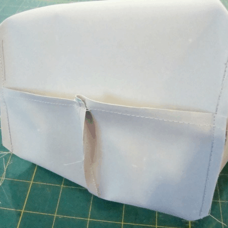 A close-up of a partially sewn fabric piece with two pockets on one side, sitting on a green cutting mat with a grid pattern. Loose threads are visible around the edges, making it perfect for a sewing tutorial on how to Sew Box Corners.