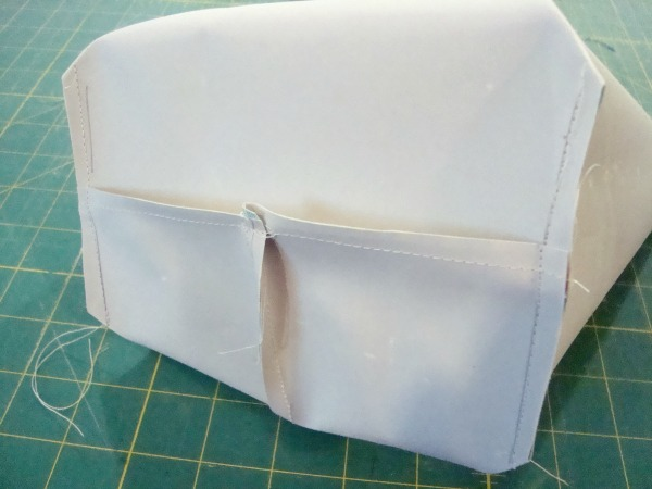 A close-up of a partially sewn fabric piece with two pockets on one side, sitting on a green cutting mat with a grid pattern. Loose threads are visible around the edges, making it perfect for a sewing tutorial on how to Sew Box Corners.
