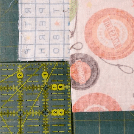 Two pieces of patterned fabric are aligned on a green cutting mat, with a transparent yellow ruler placed over the edges, measuring and aligning the fabric pieces for cutting or sewing bags, pouches, or to sew box corners.