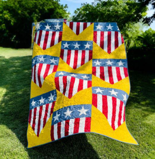 250th Anniversary Pattern Bundle - Limited Time 4 A colorful quilt from the Pattern Bundle, featuring a patriotic design with red and white stripes, blue stars, and bright yellow chevrons, is displayed outdoors on a grassy lawn—perfect for celebrating the 250th Anniversary.