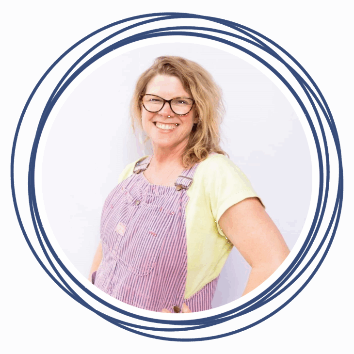 A smiling woman wearing glasses, a yellow T-shirt, and red-and-white striped overalls stands against a white background, framed by overlapping dark blue circular lines&mdash;ready to move the needle at the next quilting summit.