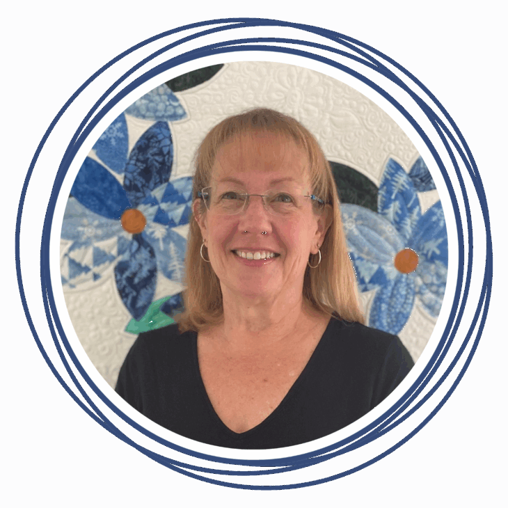 A smiling woman with glasses and shoulder-length blonde hair stands in front of a quilted background featuring blue and white flowers&mdash;perfectly capturing the artistry of machine quilting&mdash;framed by overlapping blue circles.